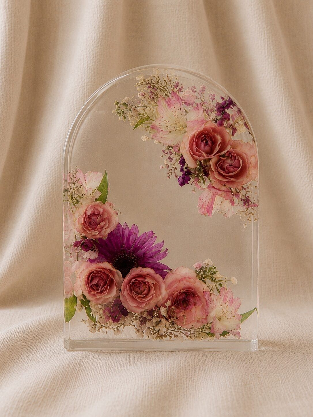 Arche en résine époxy transparente renfermant des roses blush, des alstroemerias rose pâle et de délicates fleurs préservées, présentée sur un fond de lin beige dans un style romantique et raffiné.